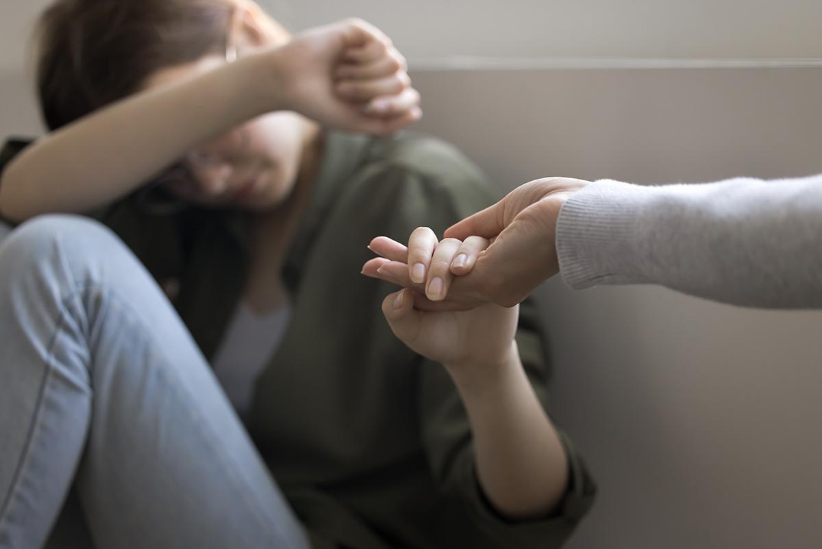 An outstretched h和 reaches into the palm of a woman who sits on the ground in distress.