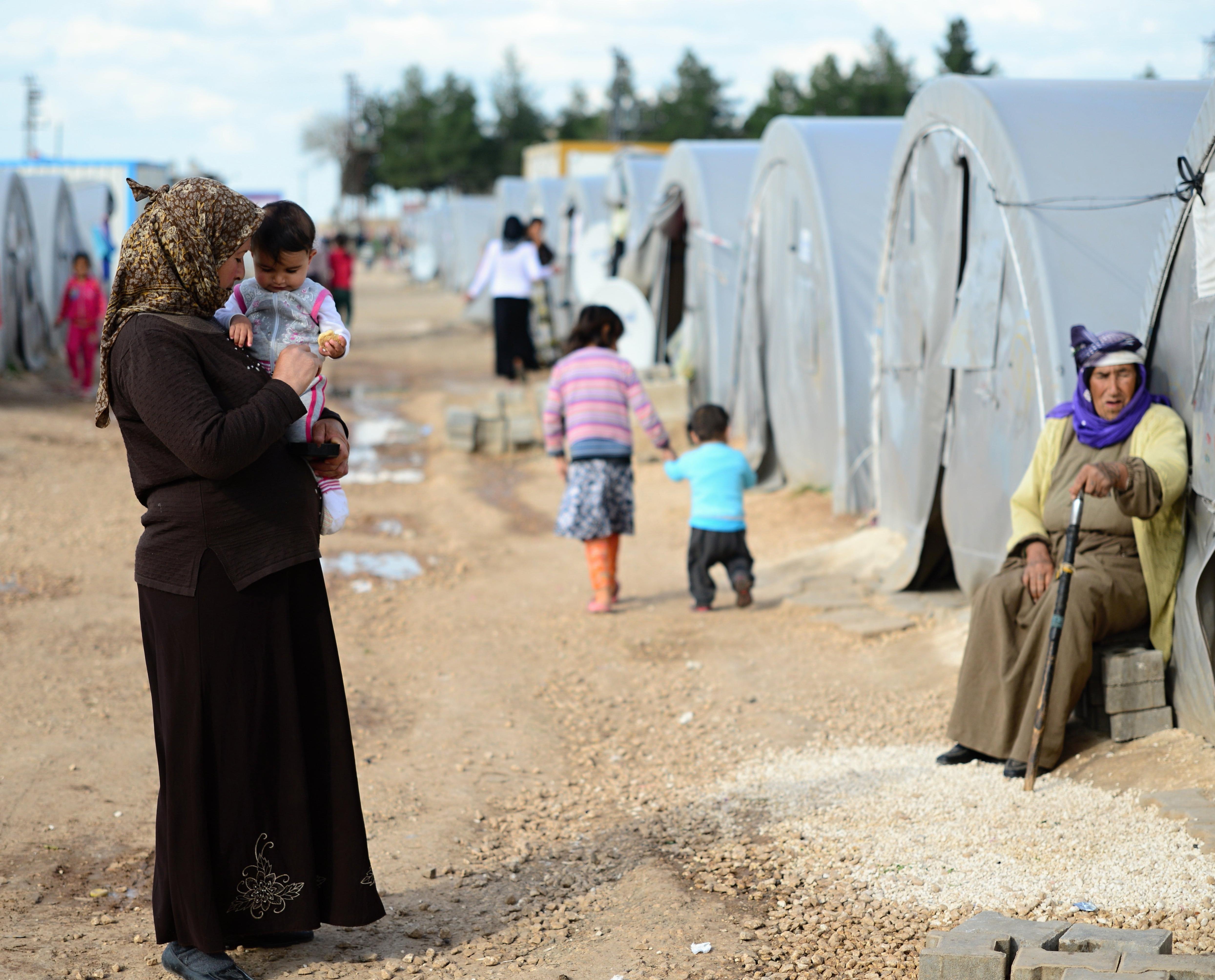 A woman st和s holding her child at a Syrian refugee camp in Turkey.